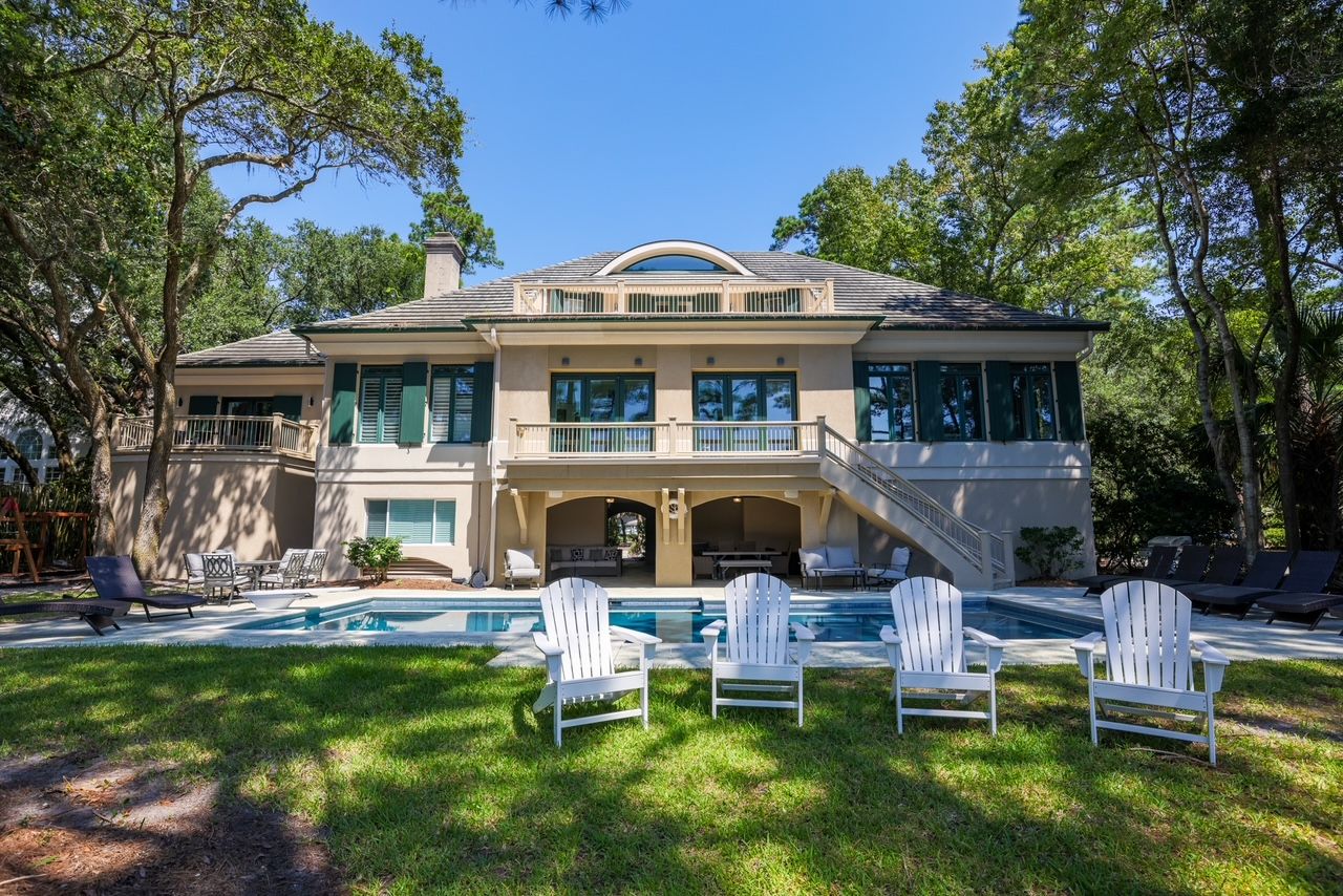 Rear of the Palmetto Dunes estate with its private pool, lawn, and white Adirondack chairs beneath the pines